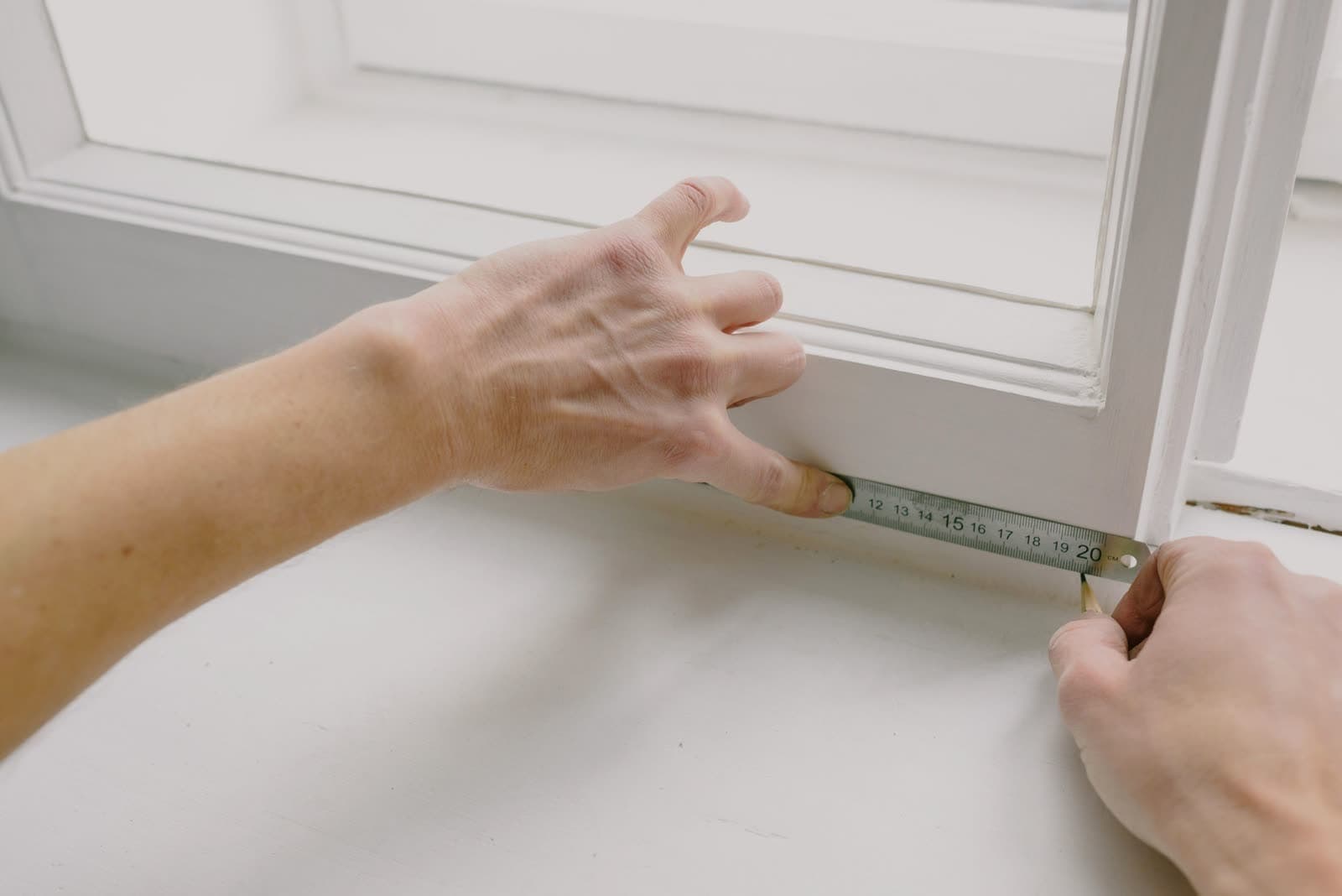 Manos midiendo con un metro el marco de una ventana pintada de blanco