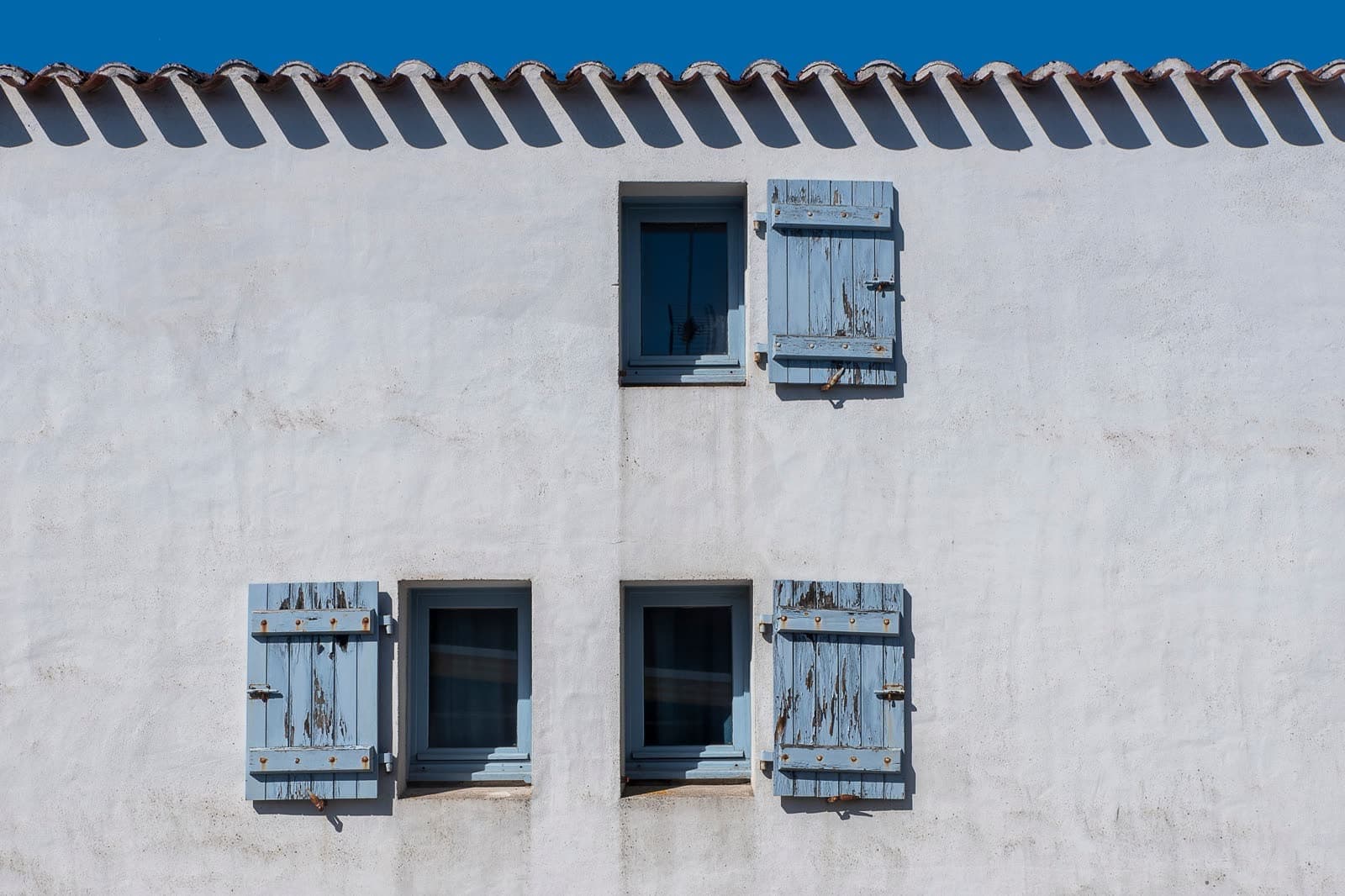 Fachada encalada con contraventanas de madera azul desgastada y cerradas
