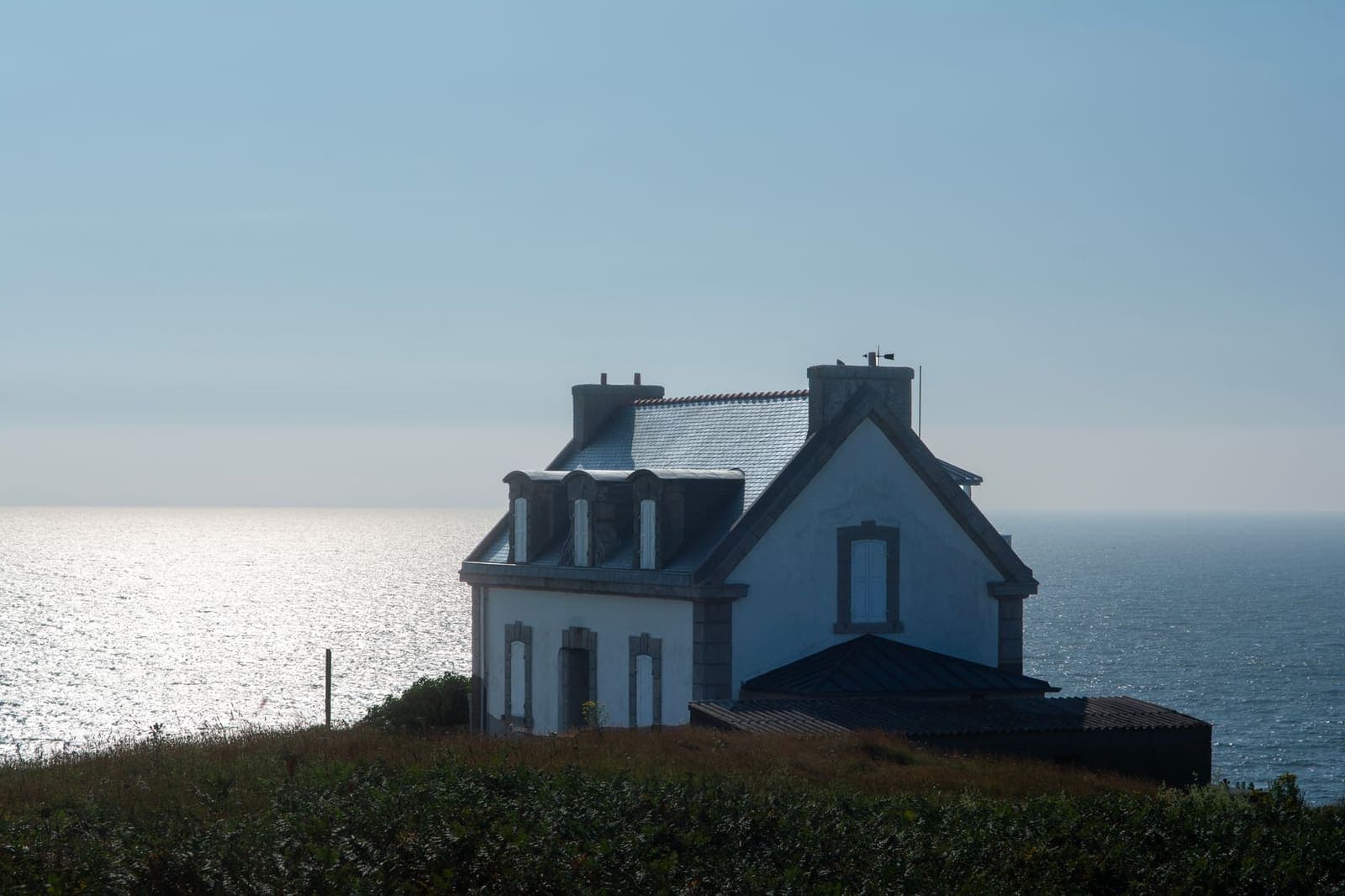 Casa de tejado de pizarra con las contraventanas cerradas, sobre un promontorio junto al mar